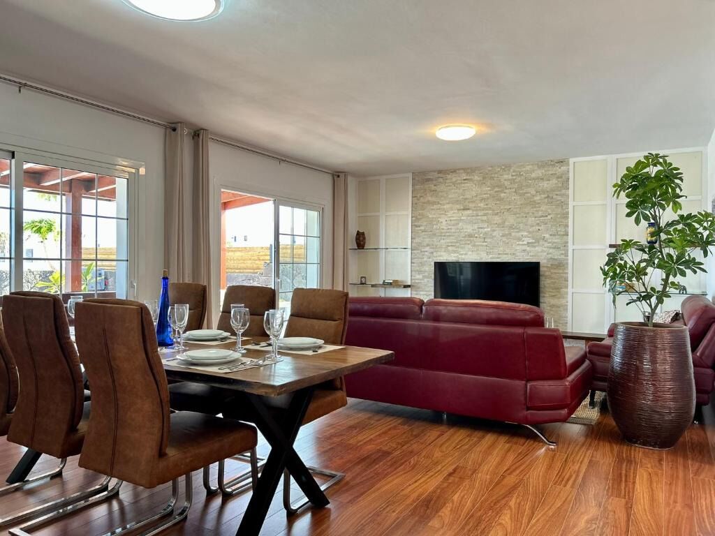 A modern living room with a dining area, a red sofa, a TV, and a large plant.