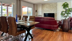 Ein modernes Wohnzimmer mit Essbereich, einem roten Sofa, einem Fernseher und einer großen Pflanze.