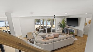 Ein modernes Wohnzimmer mit einer großen Eckcouch, einem Flachbildfernseher und Blick auf den Strand durch große Glasfenster.