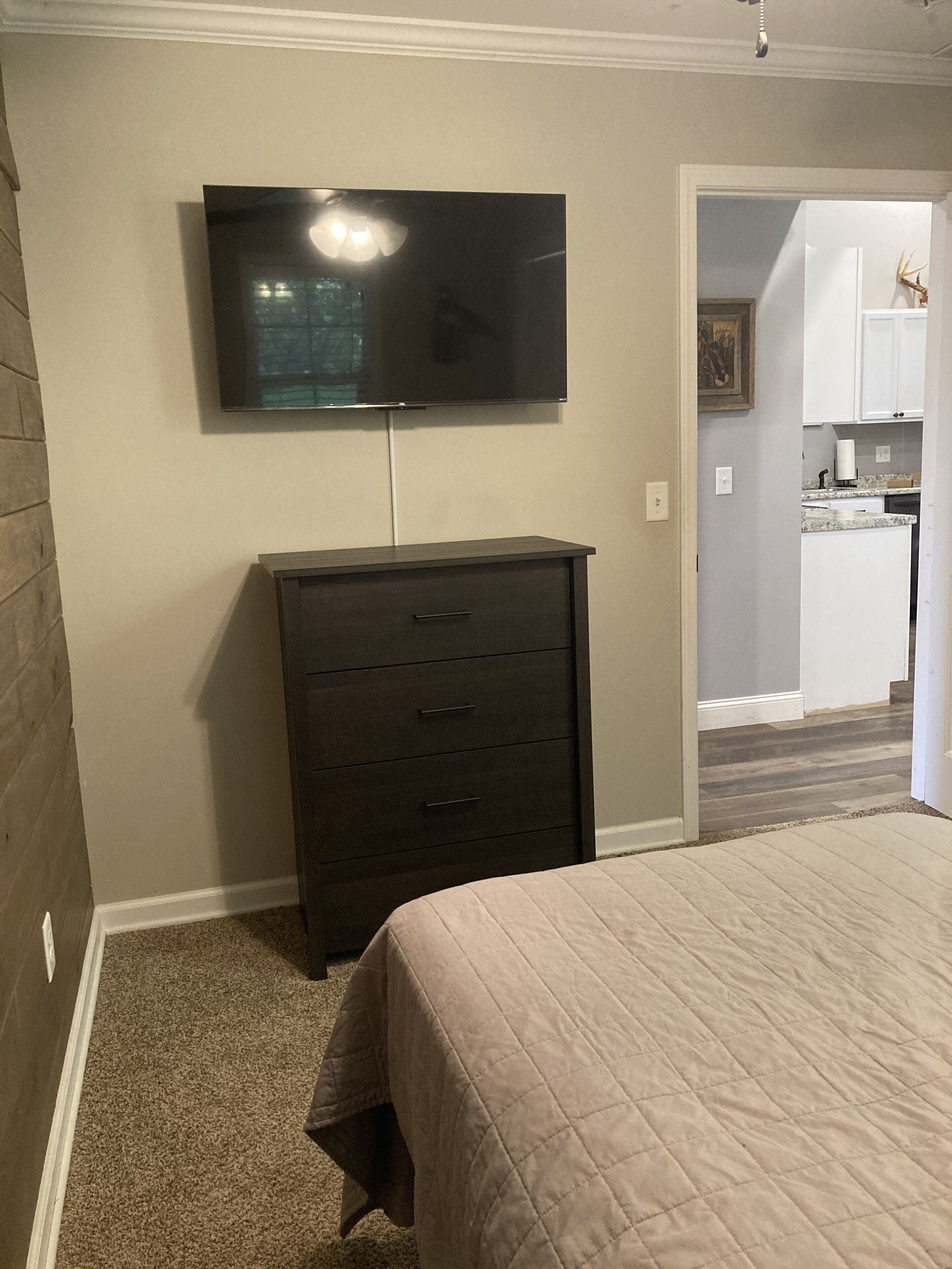 A bedroom with a bed, a dresser, and a TV mounted on the wall.