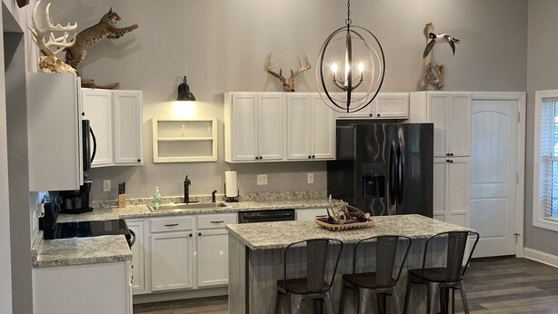 Una cocina moderna con una isla central, armarios blancos y una araña.