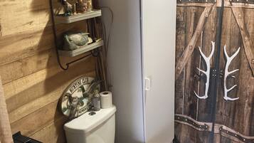 A bathroom with a wooden wall, a toilet, a white cabinet, and a shelf with various items.