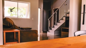 A modern interior with a wooden dining table, a cushioned seating area, a staircase, and a window with a view of greenery. - Resort Isla Cancun (Cardoso)