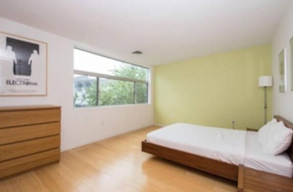 Un dormitorio con cama de madera, cómoda y ventana con vistas a la vegetación.