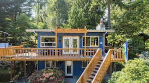 A small, blue wooden cabin with a wooden deck, a staircase, and a door. - Mid-century Beach Cabin by Avantstay Walk to Beach (Coupeville)