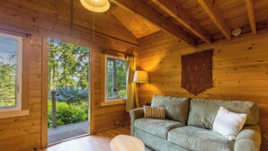 Interior de una cabaña de madera con sofá, lámpara y vistas a la vegetación.