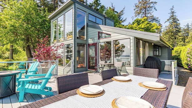 A modern house with a glass conservatory, outdoor seating, and a barbecue area.