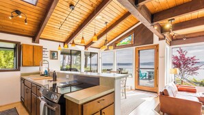 A modern kitchen with a large island, wooden ceiling beams, and large windows overlooking a scenic view.