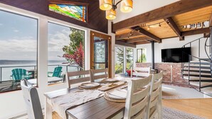 A dining area with a view of the water, a staircase, and a TV in the background.