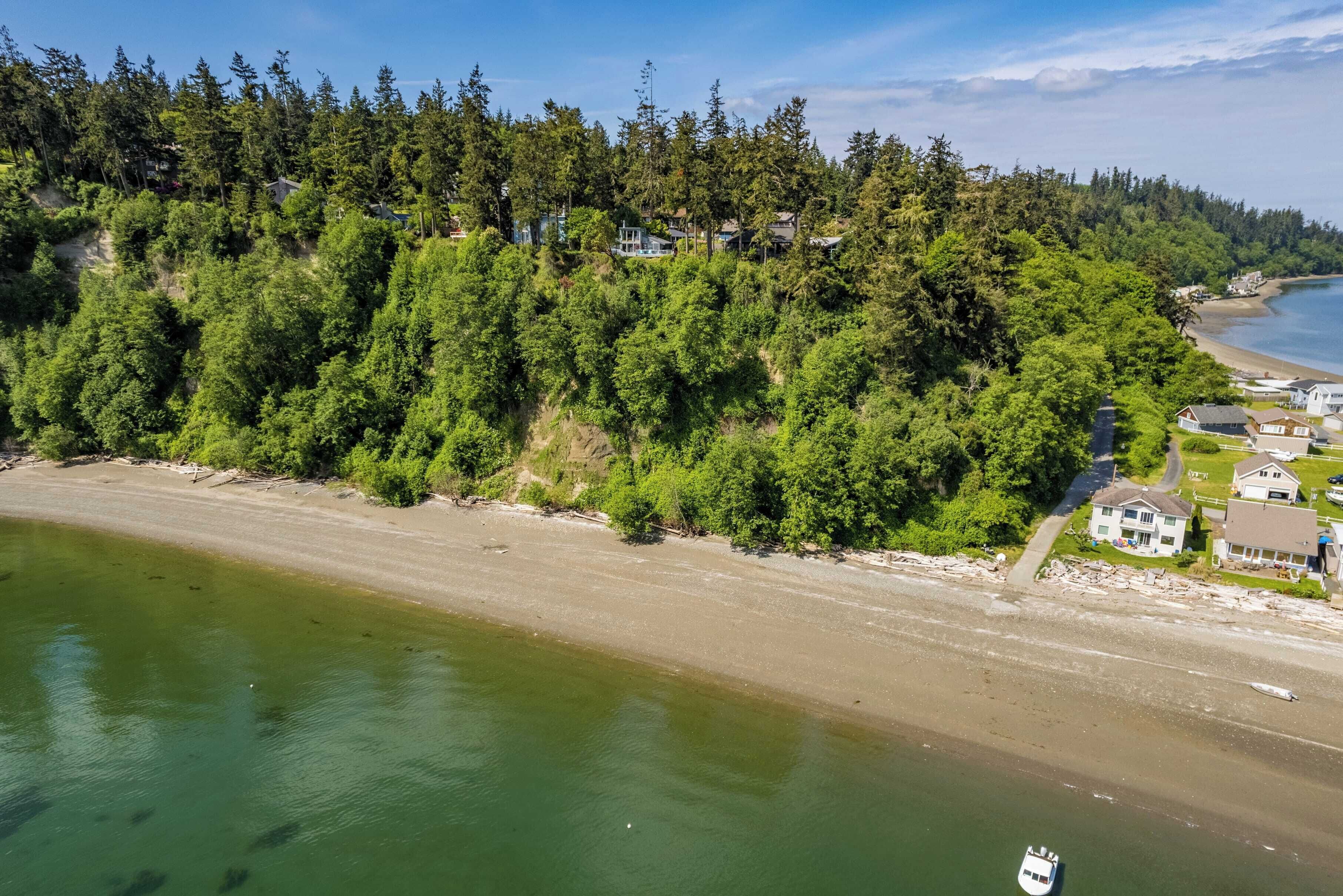 An aerial view of a coastal area with a beach, dense forest, and residential buildings.