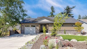 A single-story house with a garage, a stone foundation, and a landscaped front yard with various plants and flowers. - Twin Oaks Retreat by Avantstay Mins to Freeland (Freeland)