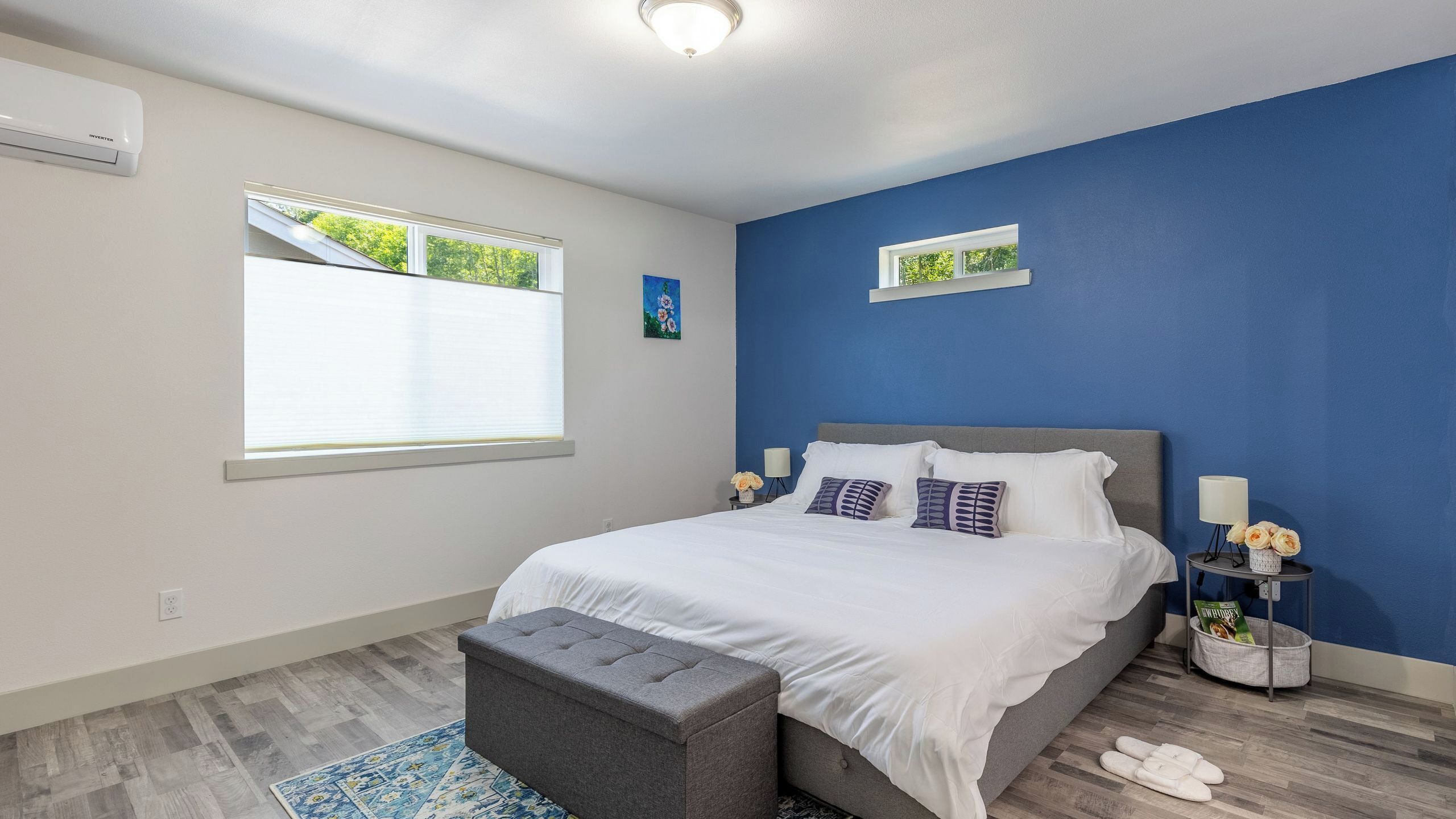 Une chambre à coucher avec un lit, un banc, une table de chevet, une lampe et une fenêtre.