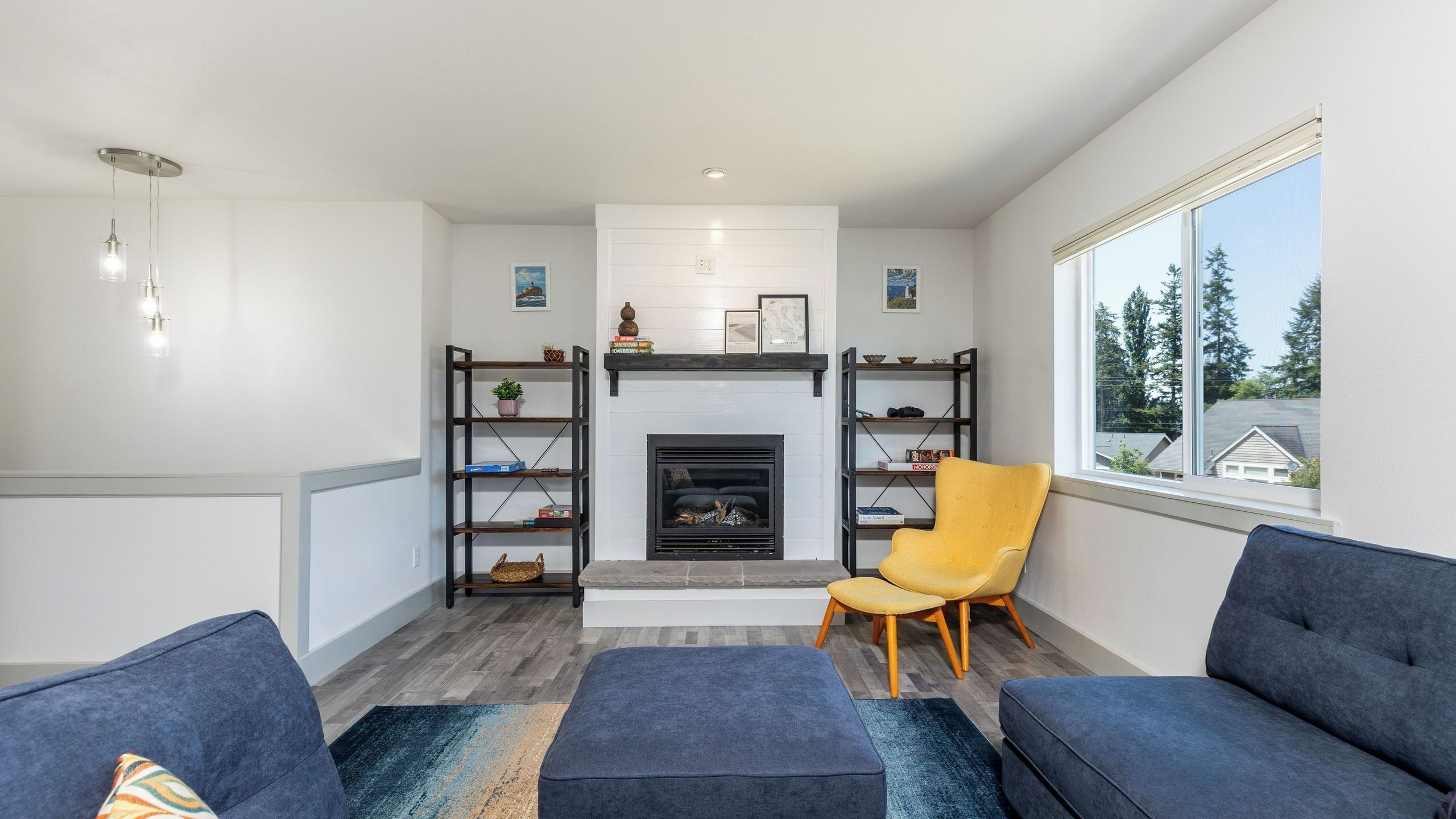 A modern living room with a fireplace, built-in bookshelves, a yellow armchair, and a large window.