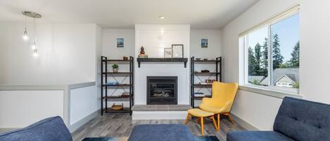 A modern living room with a fireplace, built-in bookshelves, a yellow armchair, and a large window.