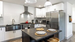 A modern kitchen with white cabinets, stainless steel appliances, and a central island with stools. - Twin Oaks Retreat by Avantstay Mins to Freeland (Freeland)