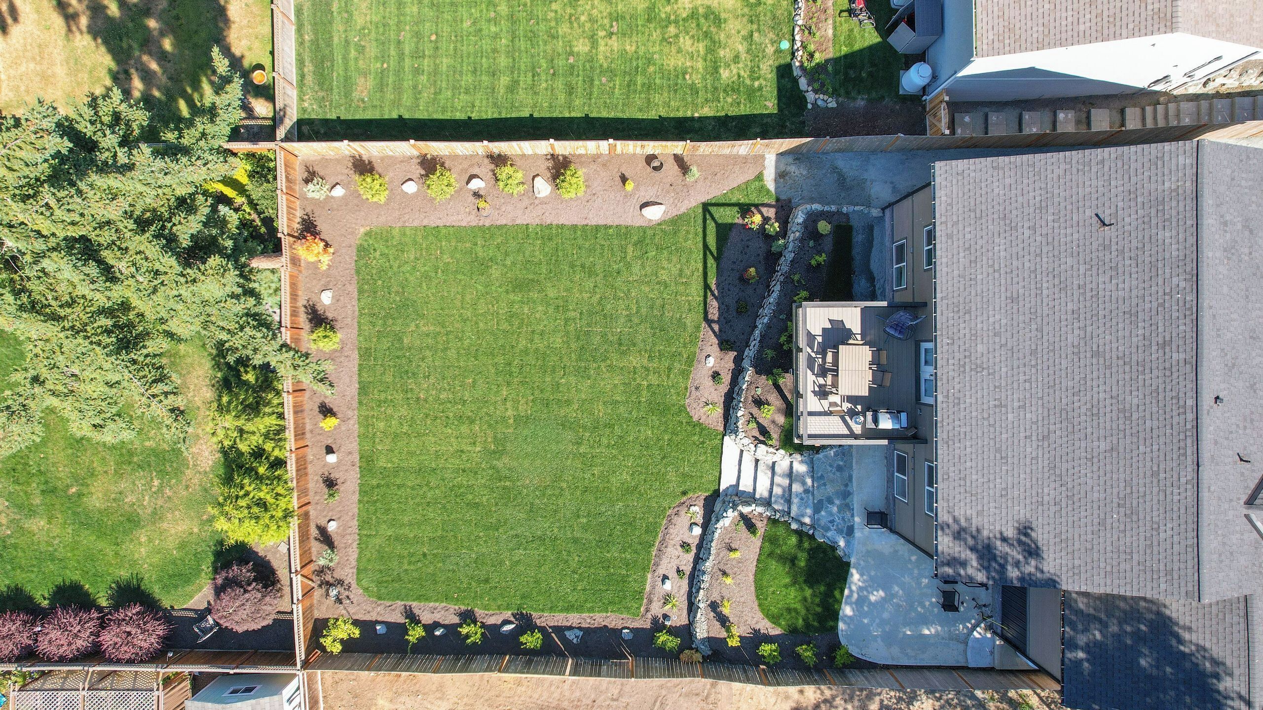 A residential property with a large lawn, a patio area with seating, and a house with a sloped roof.