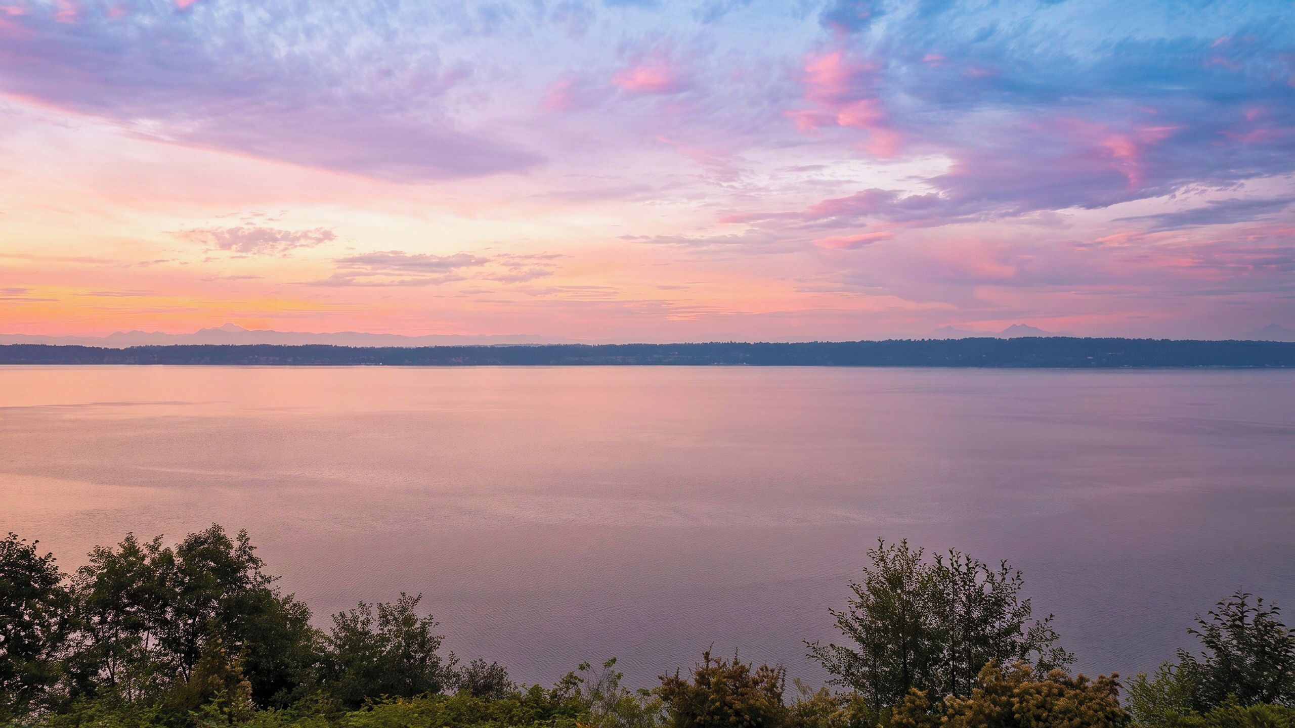 Vista panorámica de un lago tranquilo con una cadena montañosa distante y un cielo despejado.