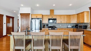 A modern kitchen with wooden cabinets, a stainless steel refrigerator, a microwave, a stove, and a large island with bar stools. - Cascade View Haven by Avantstay Saratoga Vistas (Langley)