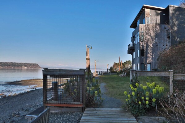 A coastal property with a wooden deck leading to a gated entrance, a view of the sea, and a modern building with large windows.