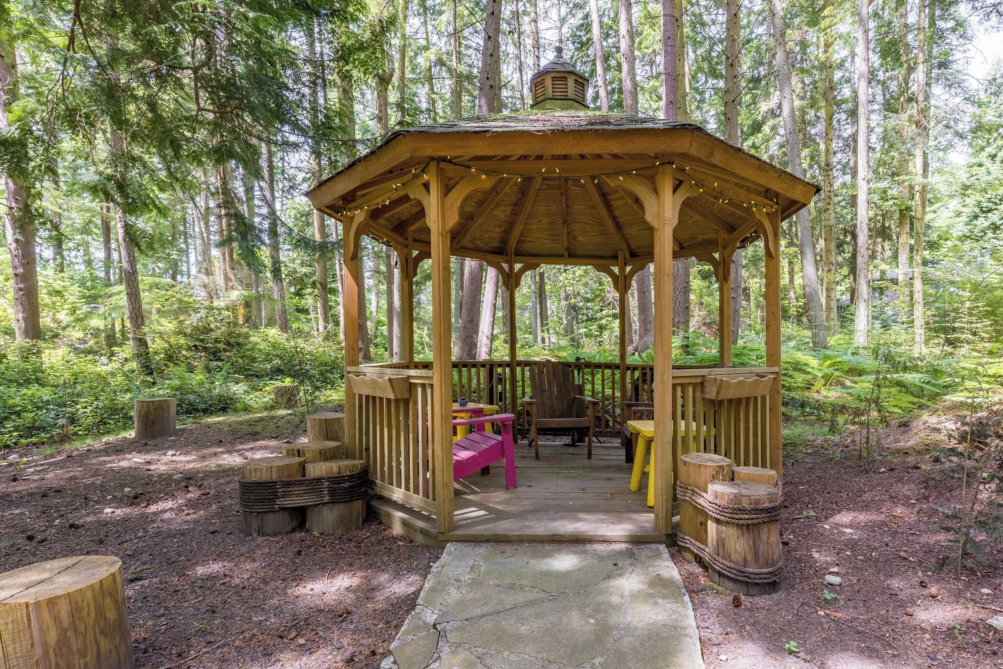 A wooden gazebo with a stone pathway leading to it, surrounded by a forest.
