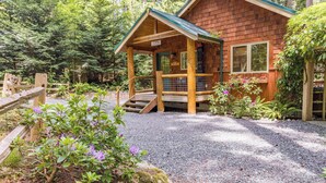 A wooden cabin with a porch, surrounded by a forest. - The Cottage at Herons Roost by Avantstay (Langley)