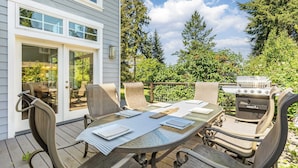 An outdoor patio with a glass-top table, metal chairs, and a grill. - Panoramic Saratoga Passage Views Elegant Whidbey Home by Avantstay (Langley)