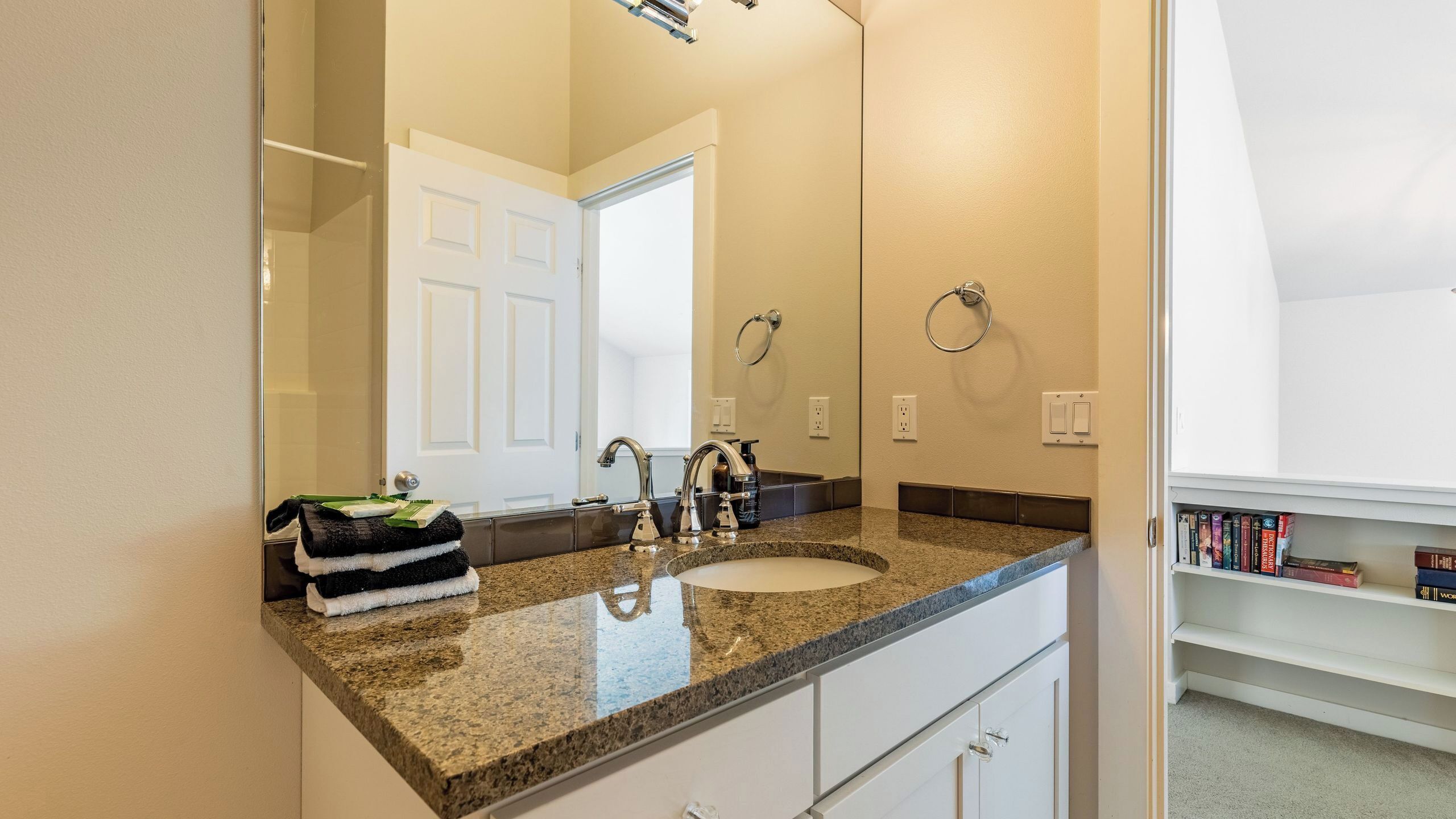 A bathroom with a granite countertop, a sink, a mirror, a towel rack, and a bookshelf with books.