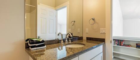 A bathroom with a granite countertop, a sink, a mirror, a towel rack, and a bookshelf with books.