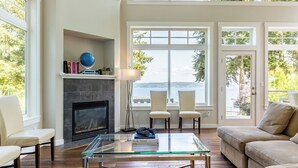 A modern living room with a fireplace, a glass coffee table, and a view of the water. - Panoramic Saratoga Passage Views Elegant Whidbey Home by Avantstay (Langley)