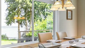 A dining table set with white plates, bowls, and cutlery, overlooking a scenic view of trees and water. - Panoramic Saratoga Passage Views Elegant Whidbey Home by Avantstay (Langley)