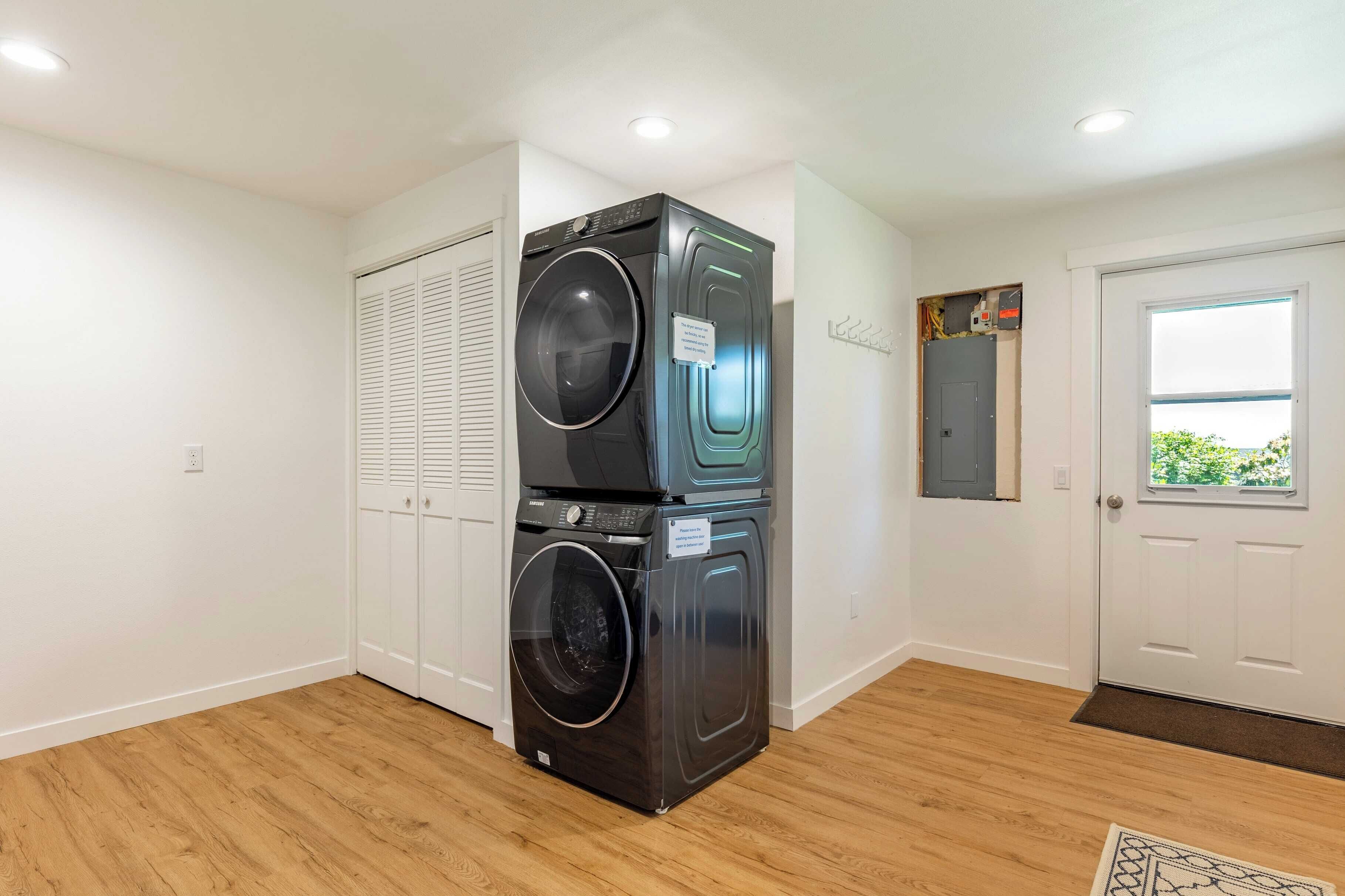 A laundry room with stacked washers and dryers, a white door, and a window with a view.