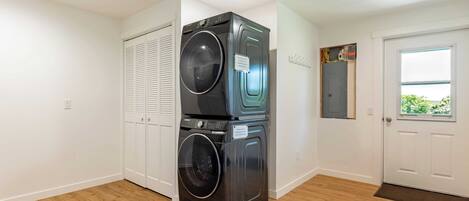 A laundry room with stacked washers and dryers, a white door, and a window with a view.