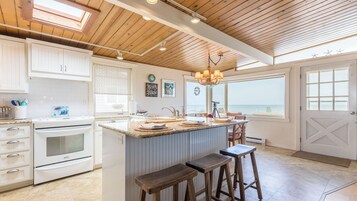 Una cocina con armarios blancos, encimera de granito y vistas al océano a través de amplios ventanales.