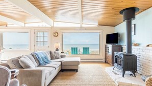 Una sala de estar acogedora con un ventanal grande que da a la playa, una chimenea y un rincón de asientos confortable.