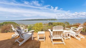 A deck with white Adirondack chairs and a small table overlooking a lake with a distant island. - Colonial Bluff House Above the Sea by Avantstay (Langley)