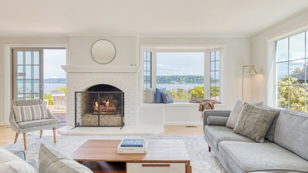 A living room with a fireplace, a sofa, a coffee table, and a view of the outdoors. - Colonial Bluff House Above the Sea by Avantstay (Langley)