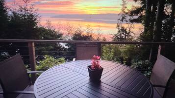 A round table with a potted plant, surrounded by chairs, overlooking a scenic view of a sunset over a body of water.