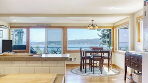 A kitchen with a large window, a dining table, chairs, and a view of the water. - Serenity Pines by Avantstay Incredible Views (Greenbank)