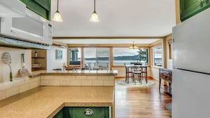 A modern kitchen with a large island, a dining area with a view, and a refrigerator. - Serenity Pines by Avantstay Incredible Views (Greenbank)