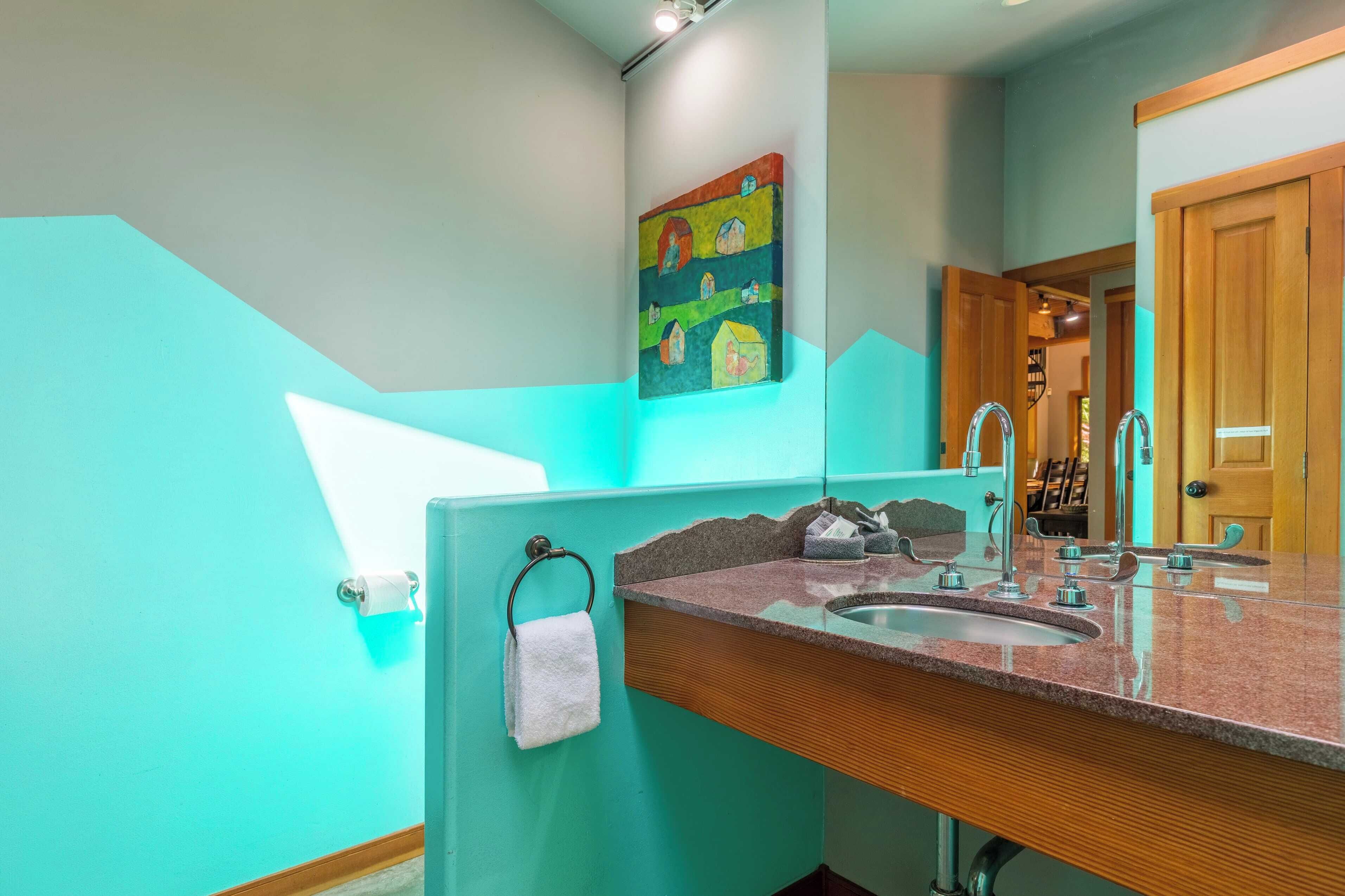 A bathroom with a turquoise wall, a wooden vanity, a sink, and a towel rack.