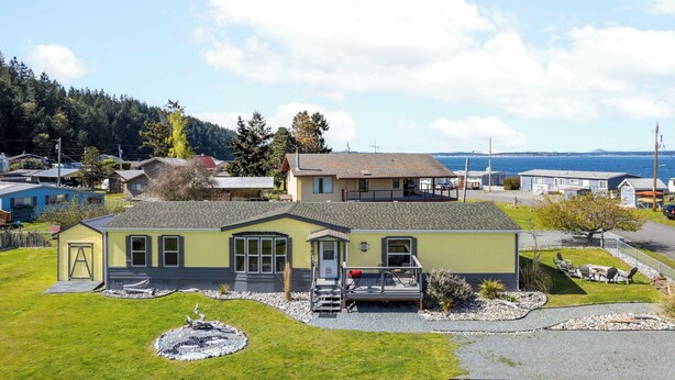 A single-story house with a front porch and a small deck, surrounded by a well-maintained lawn and a gravel driveway. - Sunny by the Sound by Avantstay Coastal Escape (Coupeville)