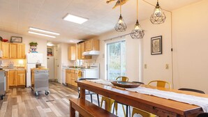 A modern kitchen with wooden cabinets, a dining table with benches, and pendant lights. - Sunny by the Sound by Avantstay Coastal Escape (Coupeville)