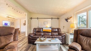 A living room with a brown leather sofa, a coffee table, and two armchairs. - Sunny by the Sound by Avantstay Coastal Escape (Coupeville)