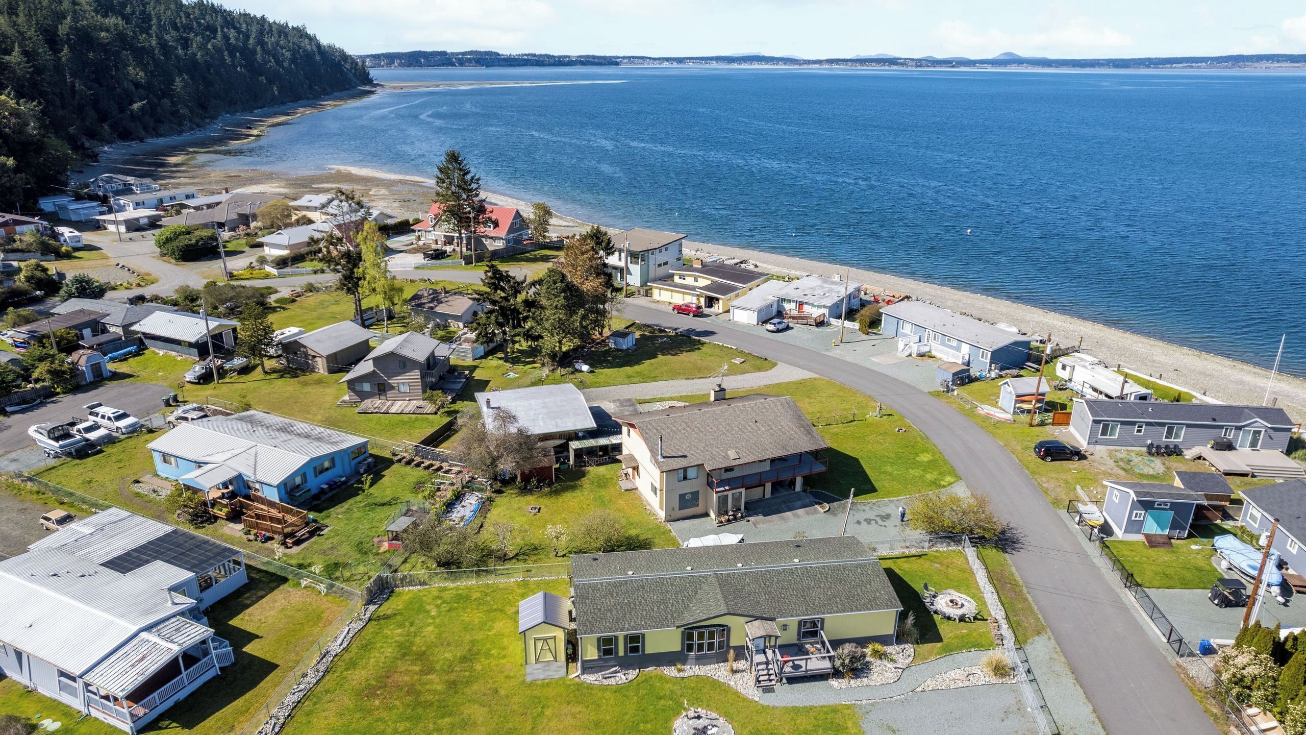 Vista aérea de una zona residencial costera con casas, una playa y un promontorio cubierto de bosque.
