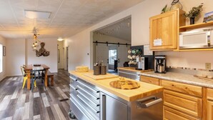 A modern kitchen with a central island, stainless steel appliances, wooden cabinets, and a dining area with a table and chairs. - Sunny by the Sound by Avantstay Coastal Escape (Coupeville)