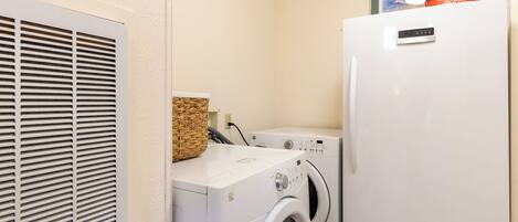 A laundry area with a white wall, a vent, a washing machine, a dryer, and a bag of Kingsford charcoal on top of the dryer.