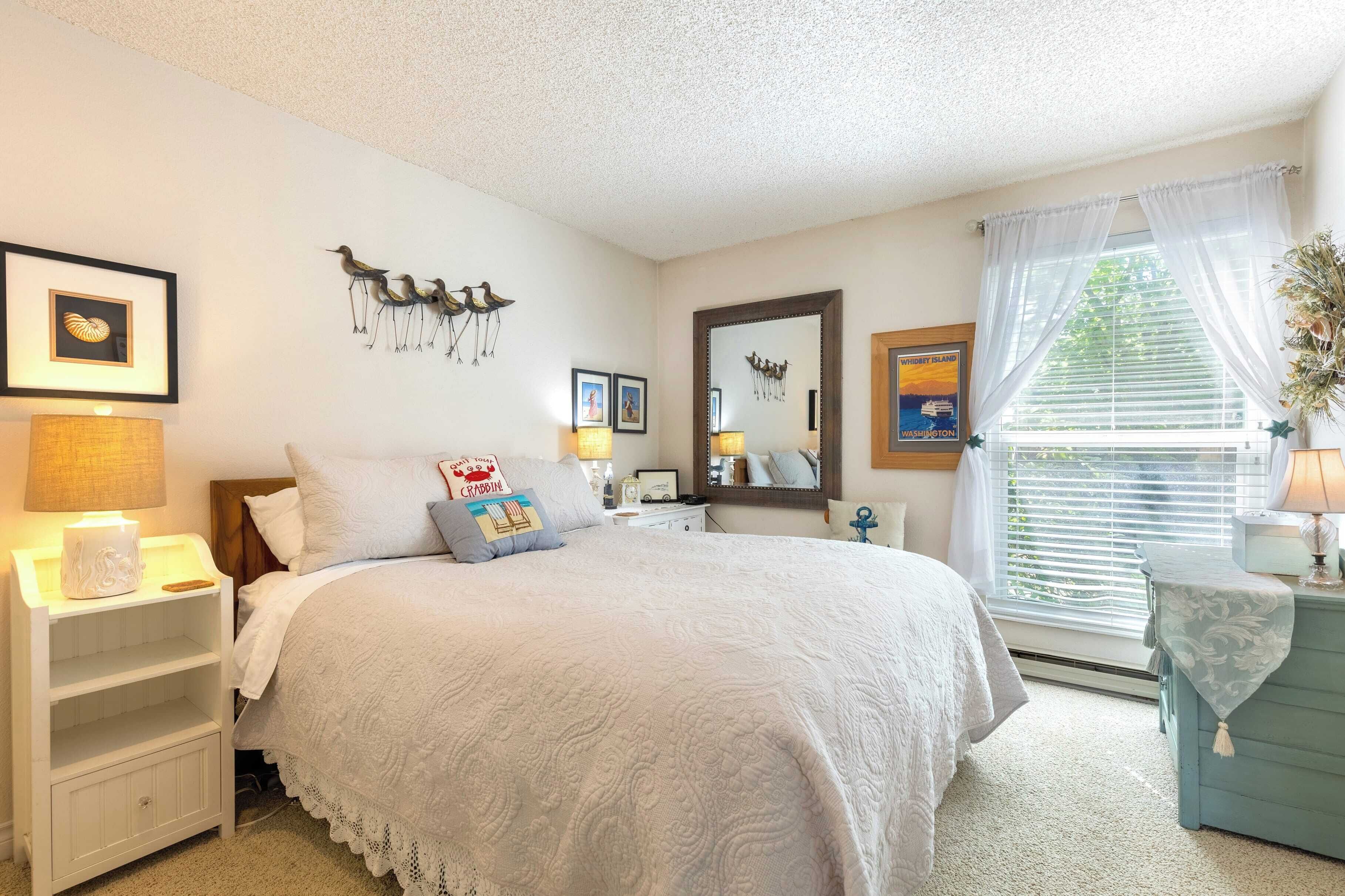 A bedroom with a large bed, a nightstand, a dresser, and a window with curtains.