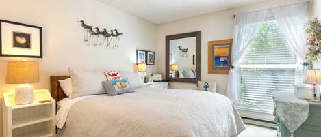 A bedroom with a large bed, a nightstand, a dresser, and a window with curtains.
