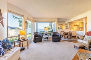 A spacious living area with a view of the ocean, a dining table, and a kitchen.