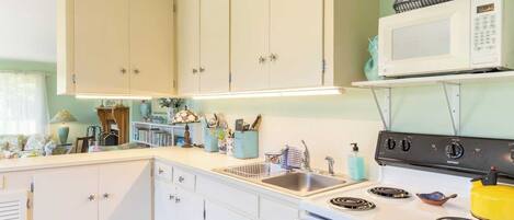 A kitchen with white cabinets, a microwave, a stove, and a sink.